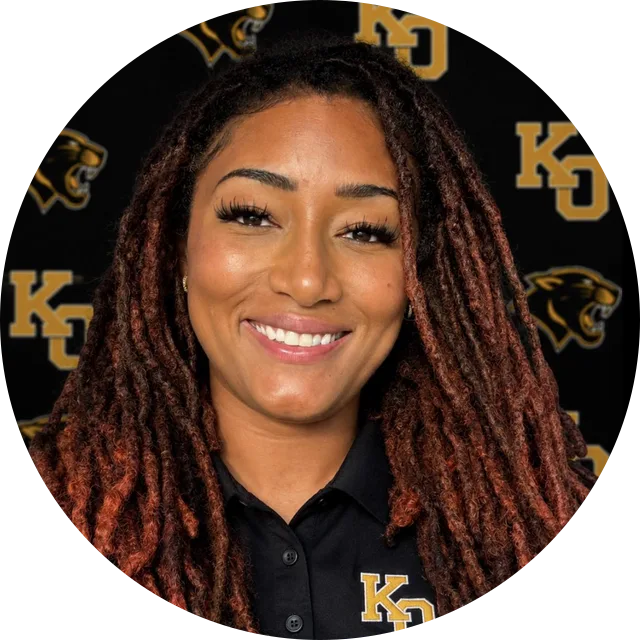 Coach Danielle Patillo in a Klein Oak polo shirt, smiling in front of a black and gold Panthers backdrop.